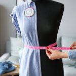 Woman's hands measuring a dressform with pink tape measure.